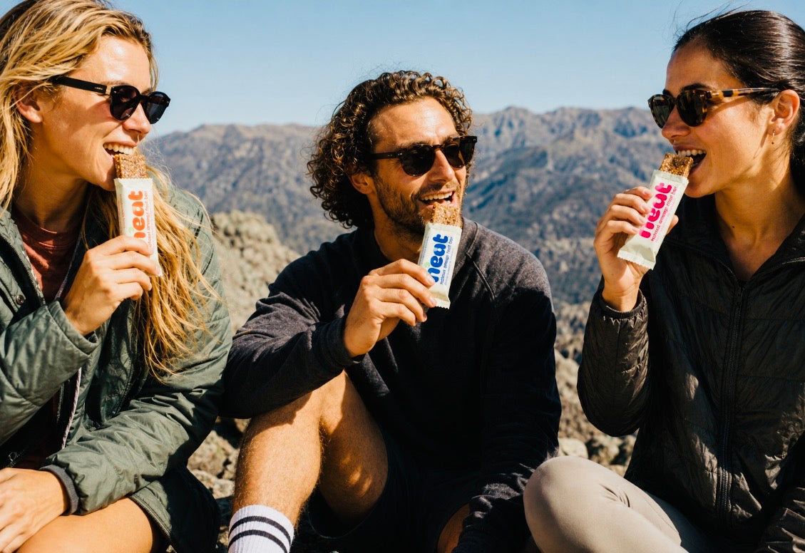Three people enjoying a N'eat energy fruit bar during an outdoor adventure